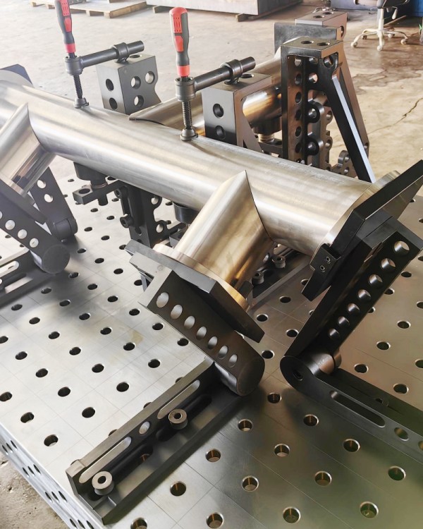 a precise pipe welding setup using the DCT 3D welding table. Modular clamps, V-blocks, and angle fixtures securely hold pipes in place, ensuring perfect alignment and stability. The nitrided table surface enhances durability, while the modular system allows efficient, repeatable welding for complex pipe assemblies.